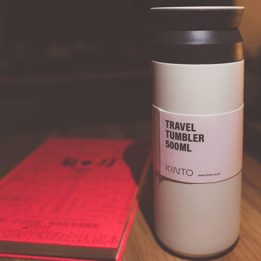 white and black Kinto travel tumbler beside red covered book