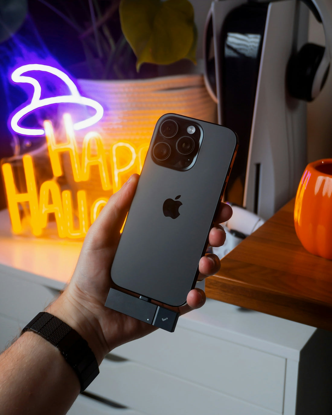 Hand holding a dark iPhone with a halloween decoration.