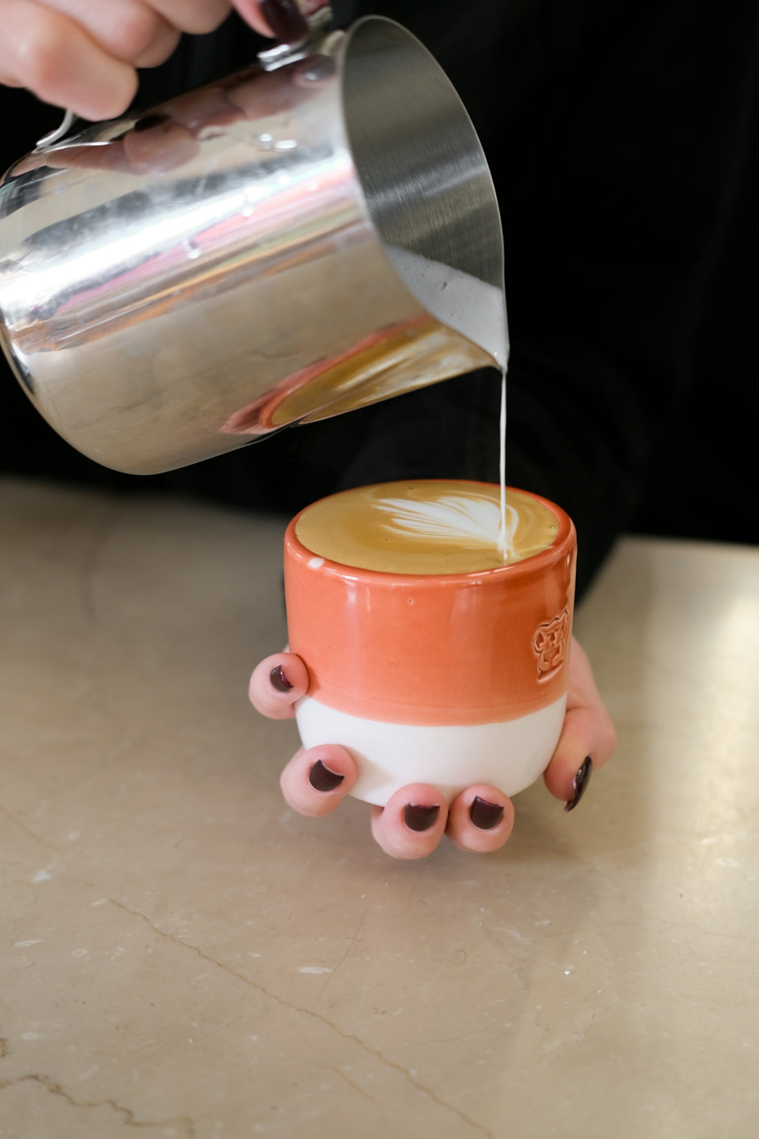 Barista pouring steamed milk into coffee for latte art.