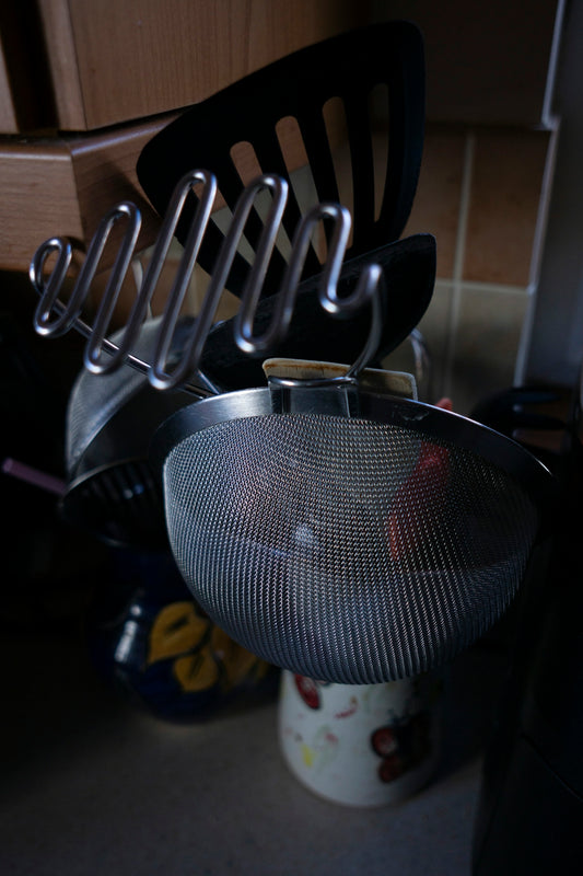 Metal strainer, slotted spatula, and potato masher in a kitchen.