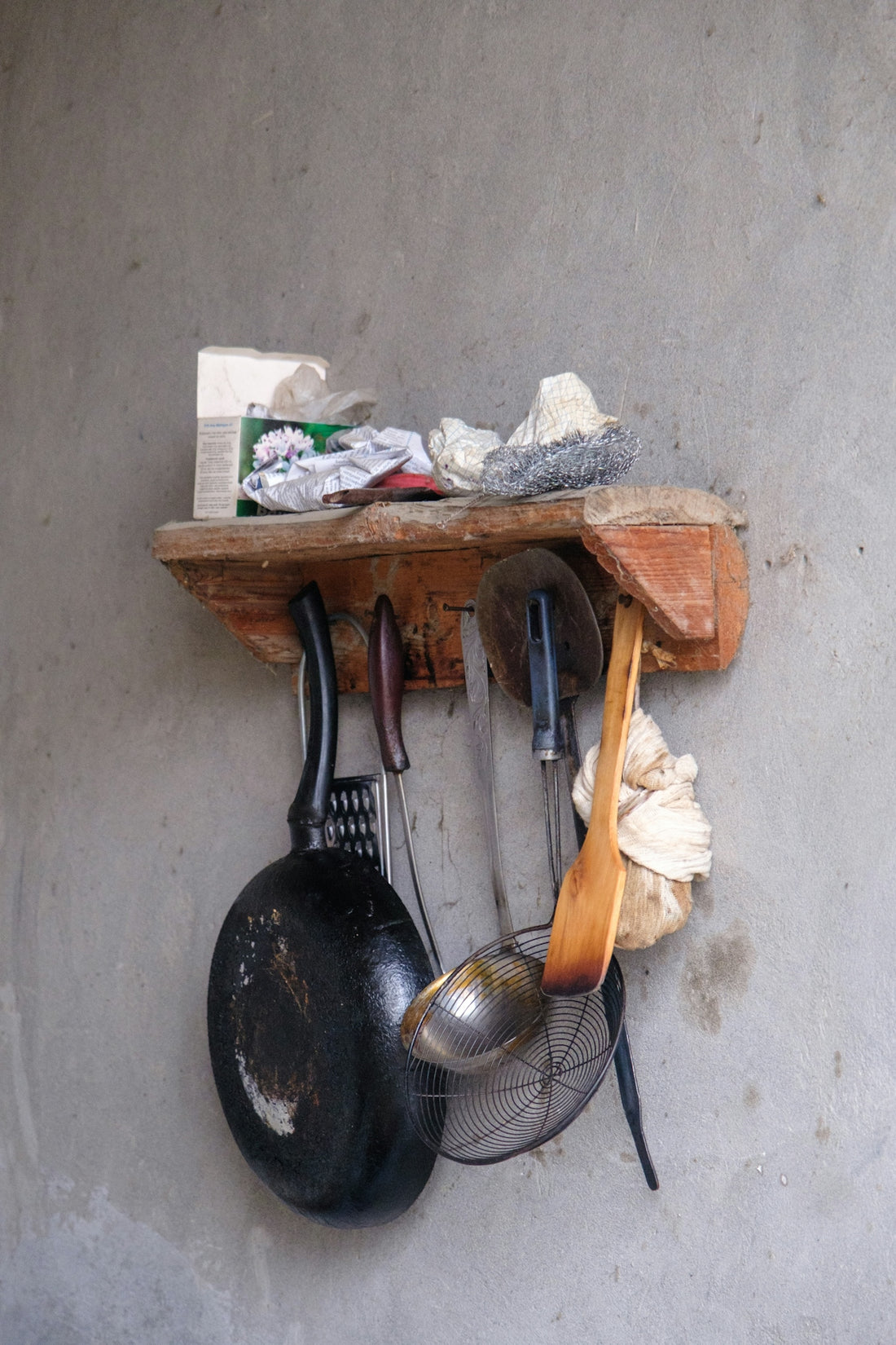 Various kitchen tools hanging from a rustic wooden shelf.