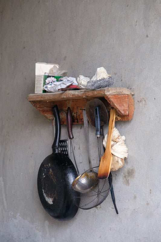 Various kitchen tools hanging from a rustic wooden shelf.