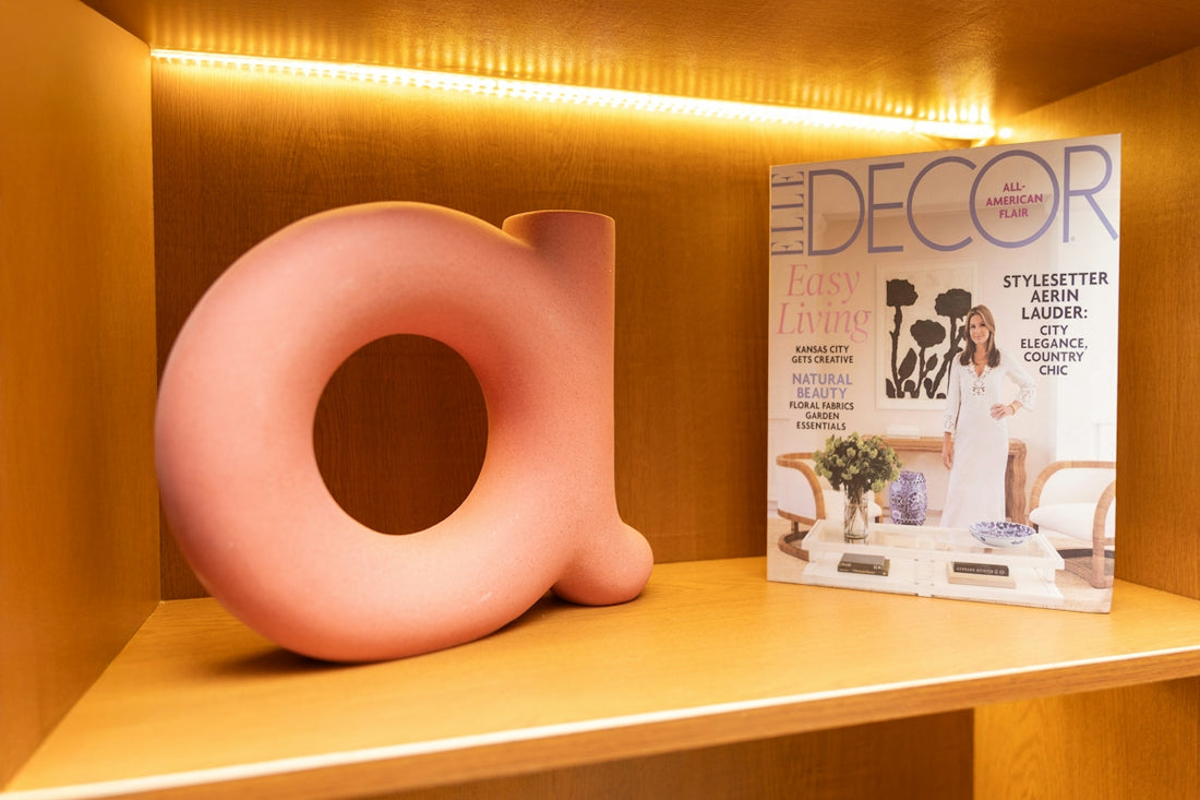 Pink 'a' decor and magazine on a lit wooden shelf