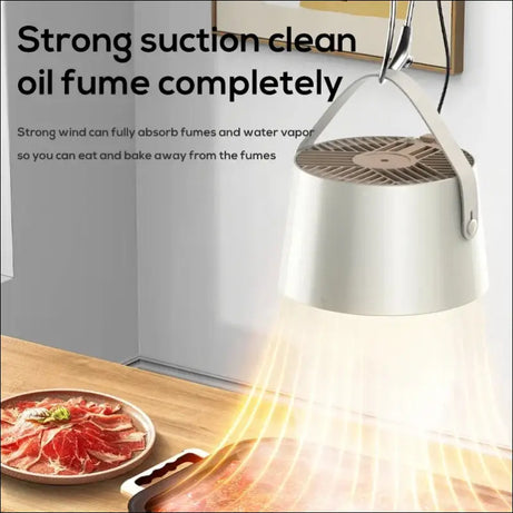 Portable fan suctioning oil fumes above grill for smoke-free cooking.