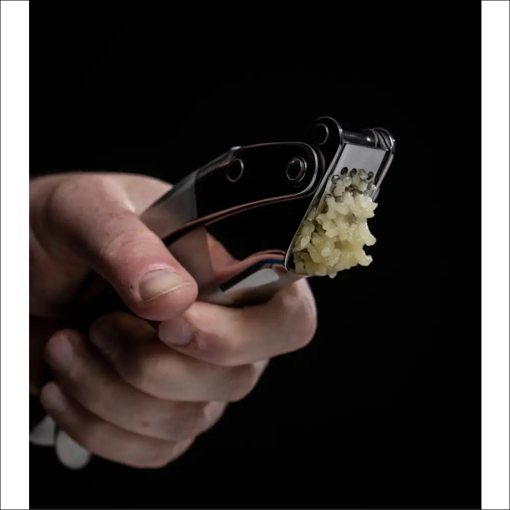 Hand holding a garlic crusher with crushed garlic showing the ProPress garlic.